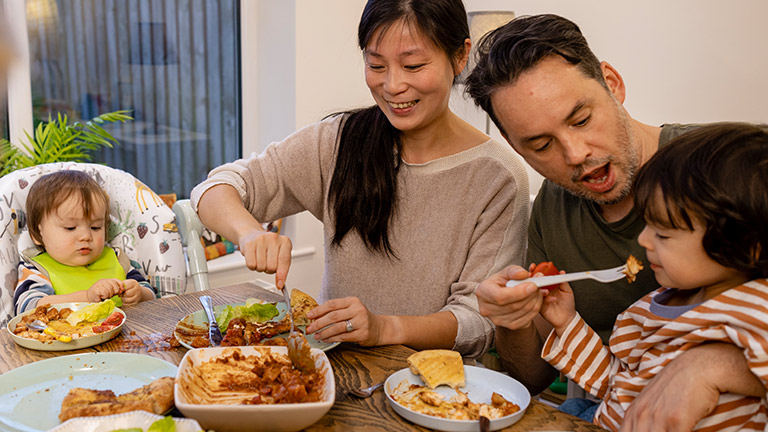 Mother and father with two young children eating dinner.