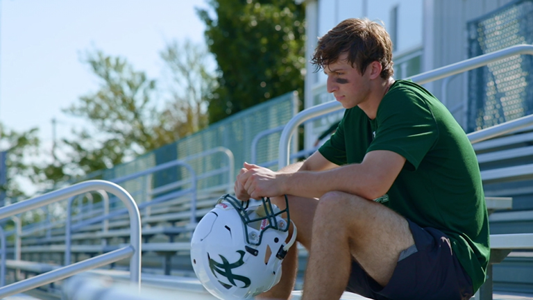 Youth school football player sitting and thinking.